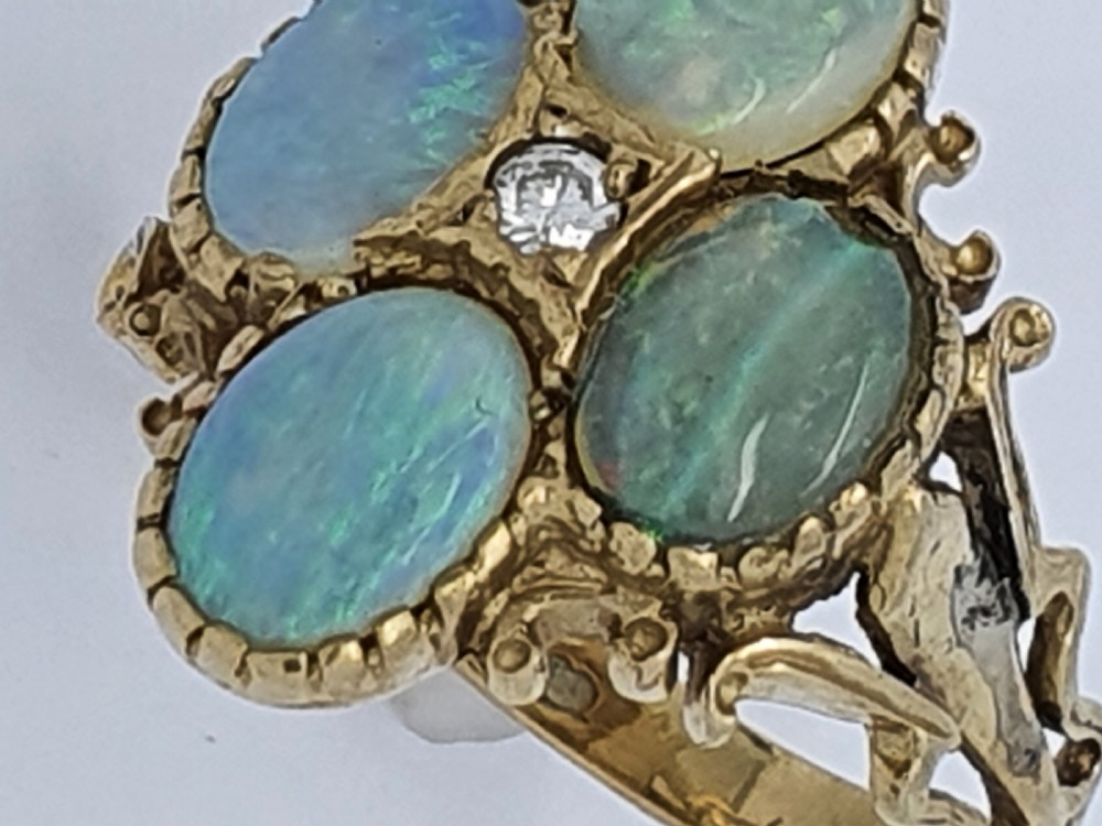 A 9ct yellow gold dress ring featuring four oval cabochon opals arranged in a cluster around a central brilliant-cut diamond, mounted on an ornate scrollwork band. View III