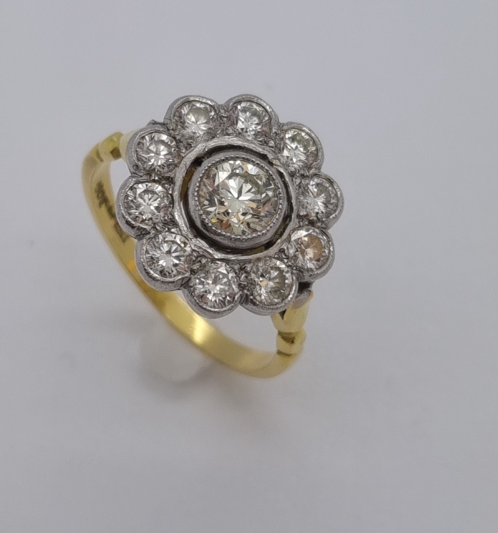 An antique diamond cluster ring featuring a central round diamond encircled by ten smaller diamonds set in a white metal head with a yellow gold band.
