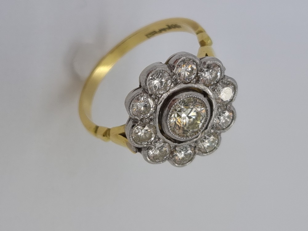 An antique diamond cluster ring featuring a central round diamond encircled by ten smaller diamonds set in a white metal head with a yellow gold band. View II