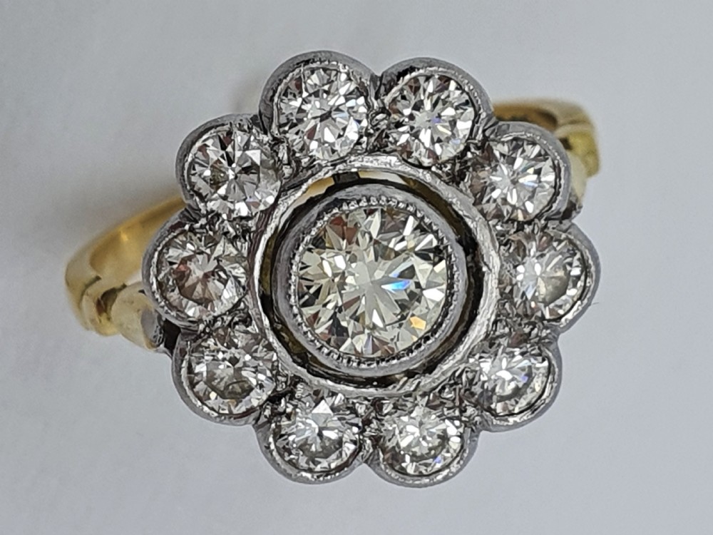 An antique diamond cluster ring featuring a central round diamond encircled by ten smaller diamonds set in a white metal head with a yellow gold band. View VI