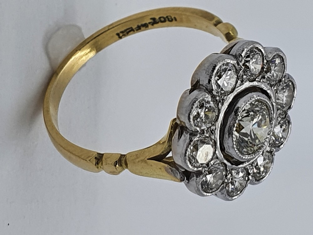 An antique diamond cluster ring featuring a central round diamond encircled by ten smaller diamonds set in a white metal head with a yellow gold band. View VII