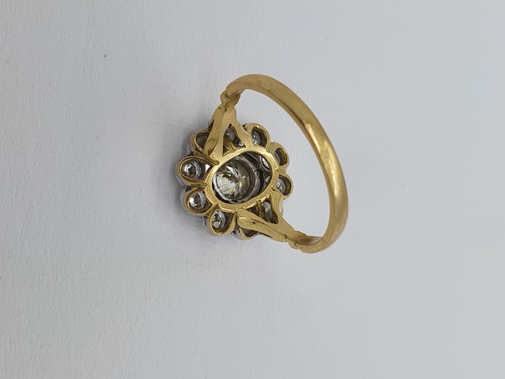 An antique diamond cluster ring featuring a central round diamond encircled by ten smaller diamonds set in a white metal head with a yellow gold band. View VIII