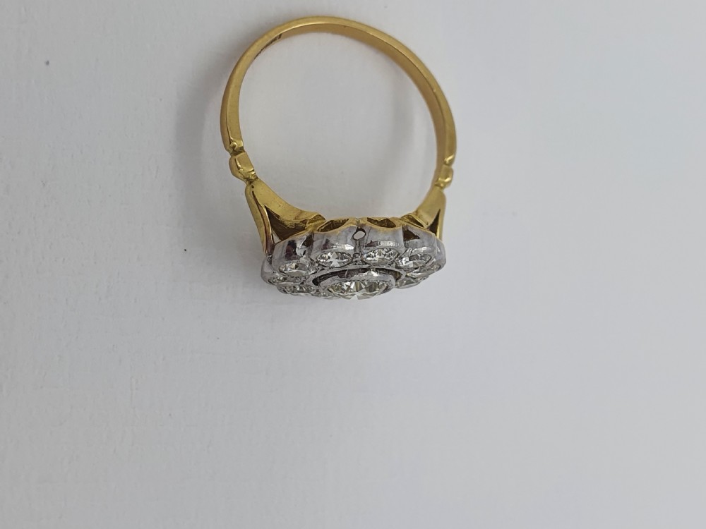 An antique diamond cluster ring featuring a central round diamond encircled by ten smaller diamonds set in a white metal head with a yellow gold band. View X