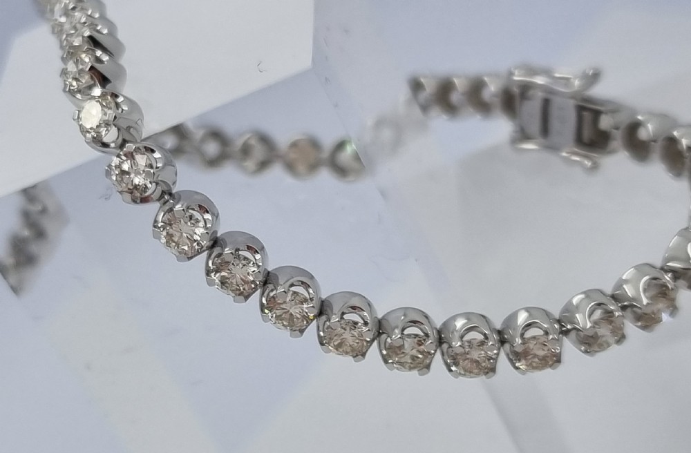 A flexible collet set diamond tennis bracelet crafted in white metal with a continuous row of round brilliant cut diamonds. View VI