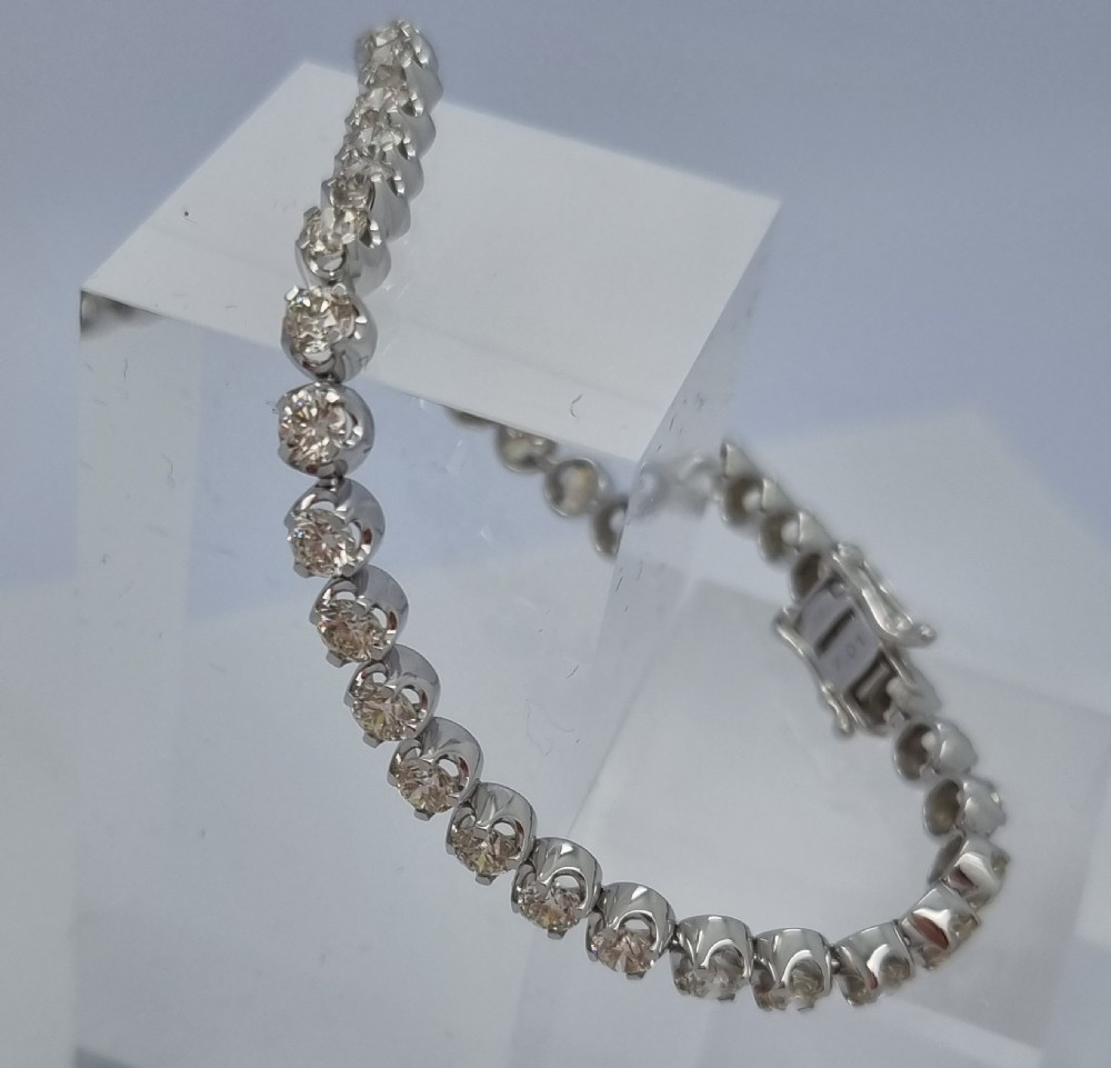 A flexible collet set diamond tennis bracelet crafted in white metal with a continuous row of round brilliant cut diamonds. View IX