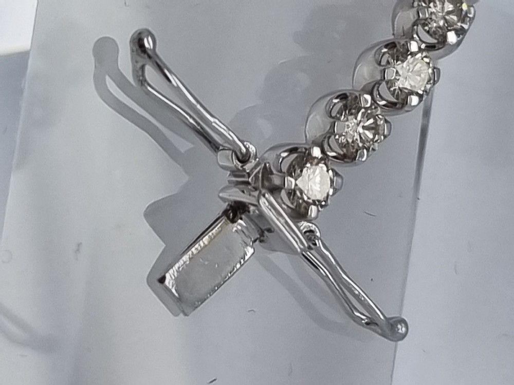 A flexible collet set diamond tennis bracelet crafted in white metal with a continuous row of round brilliant cut diamonds. View XI