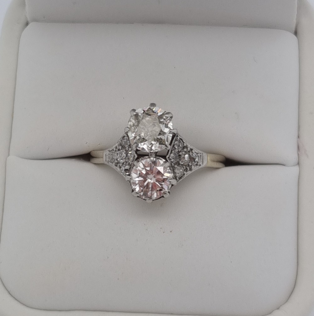 An Art Deco period two-stone diamond ring featuring vertically set principal stones flanked by pave-set diamond shoulders.