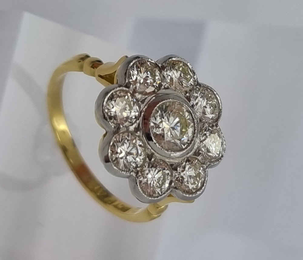 An 18ct yellow gold ring featuring a platinum-set floral head diamond cluster with a central round diamond encircled by eight surrounding diamonds.