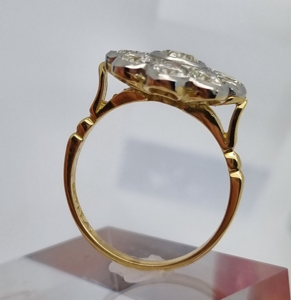 An 18ct yellow gold ring featuring a platinum-set floral head diamond cluster with a central round diamond encircled by eight surrounding diamonds. View V