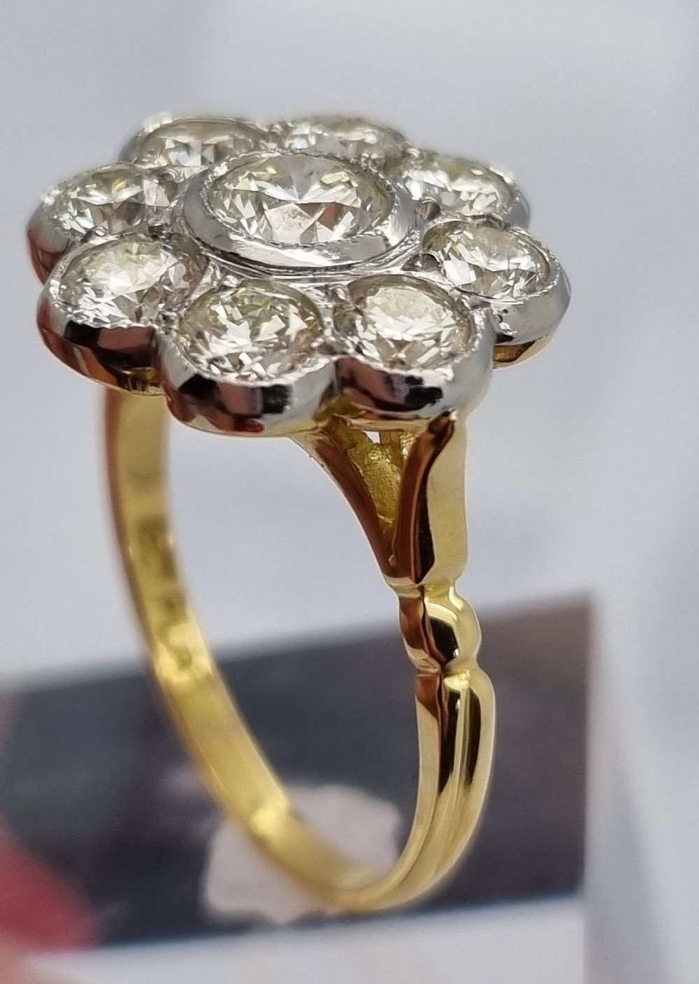 An 18ct yellow gold ring featuring a platinum-set floral head diamond cluster with a central round diamond encircled by eight surrounding diamonds. View VIII