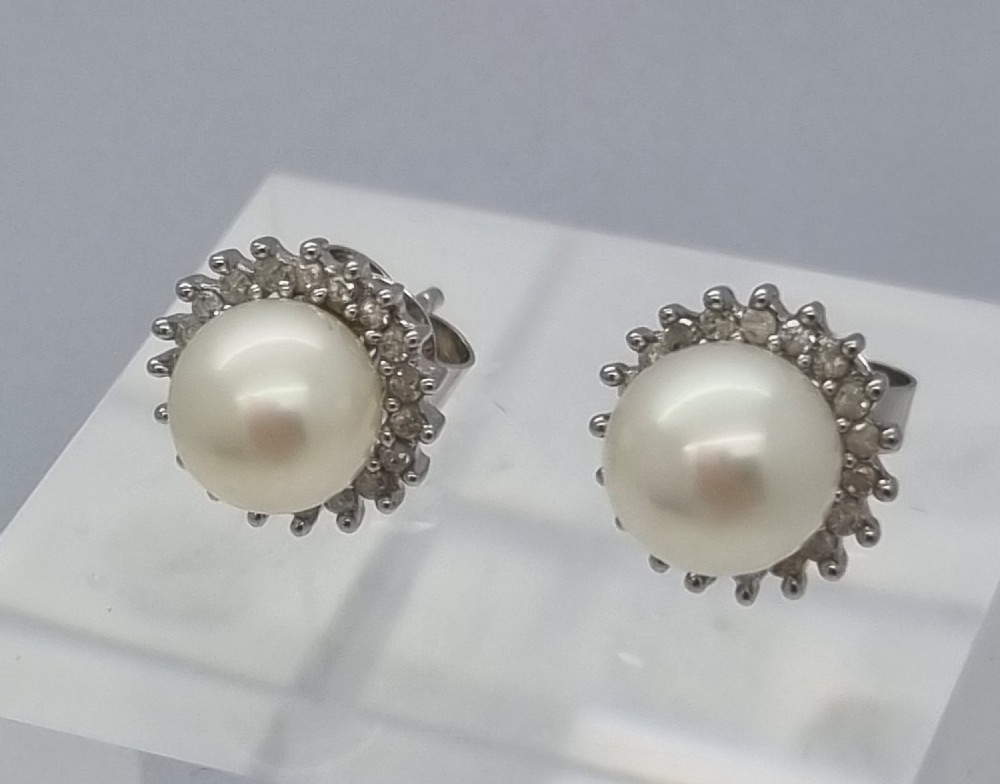 A pair of 9ct white gold stud earrings featuring round cream central pearls surrounded by halos of small round diamonds.