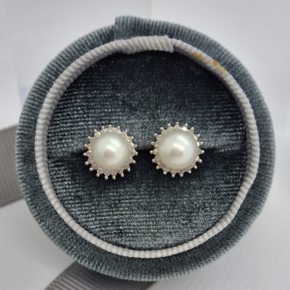 A pair of 9ct white gold stud earrings featuring round cream central pearls surrounded by halos of small round diamonds. View VII