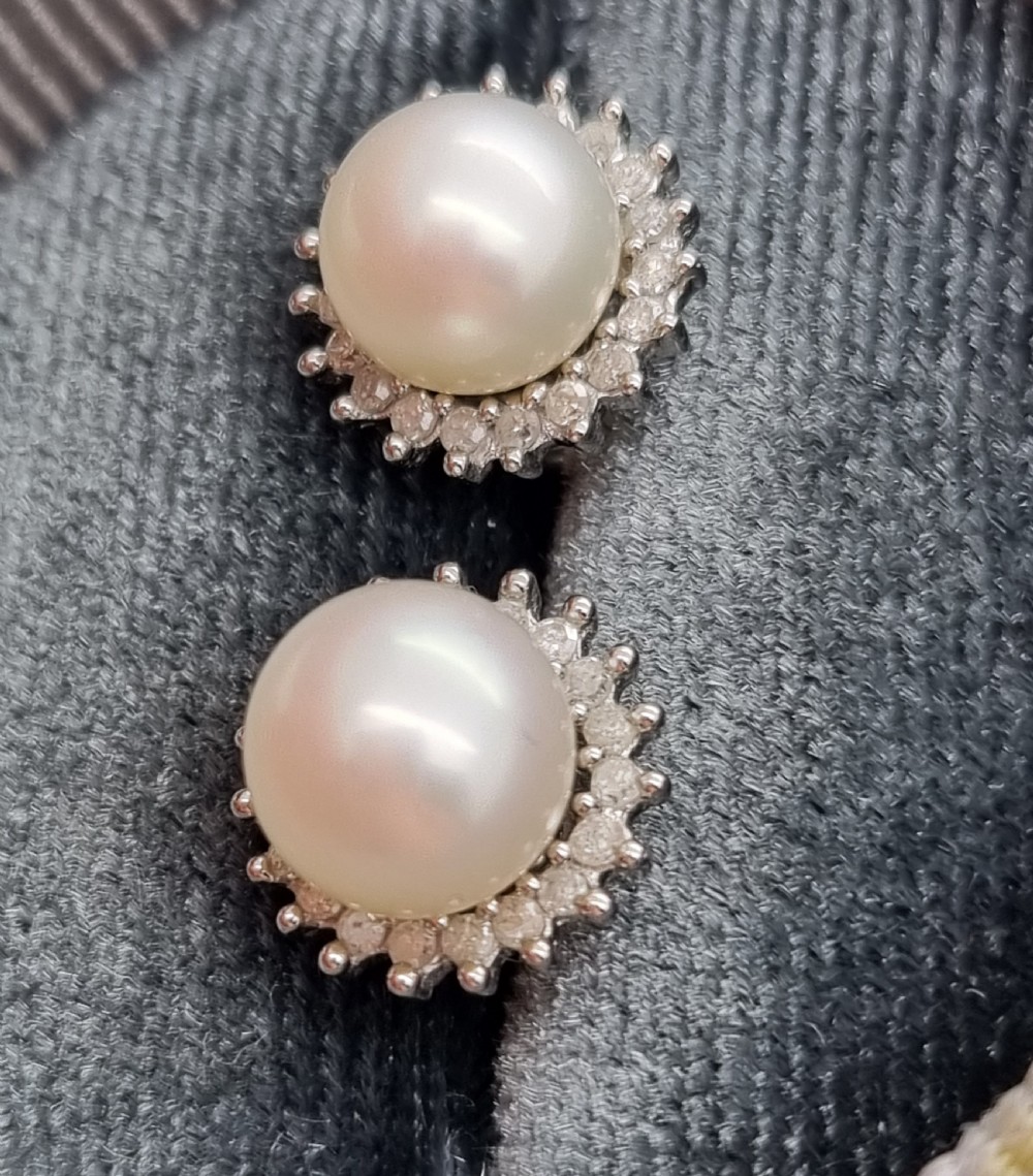 A pair of 9ct white gold stud earrings featuring round cream central pearls surrounded by halos of small round diamonds. View VIII