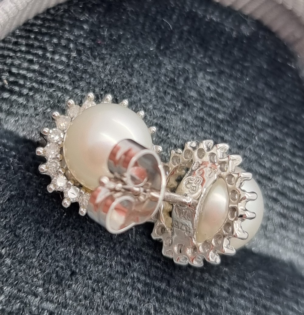 A pair of 9ct white gold stud earrings featuring round cream central pearls surrounded by halos of small round diamonds. View IX