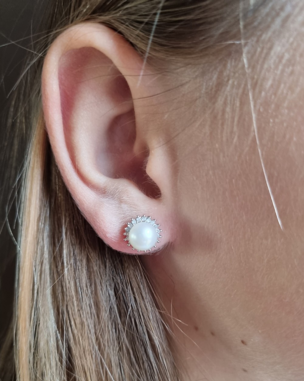 A pair of 9ct white gold stud earrings featuring round cream central pearls surrounded by halos of small round diamonds. View X