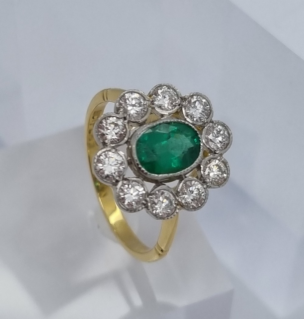 An oval-cut green emerald surrounded by a halo of ten round diamonds in a millgrained cluster setting. View IV