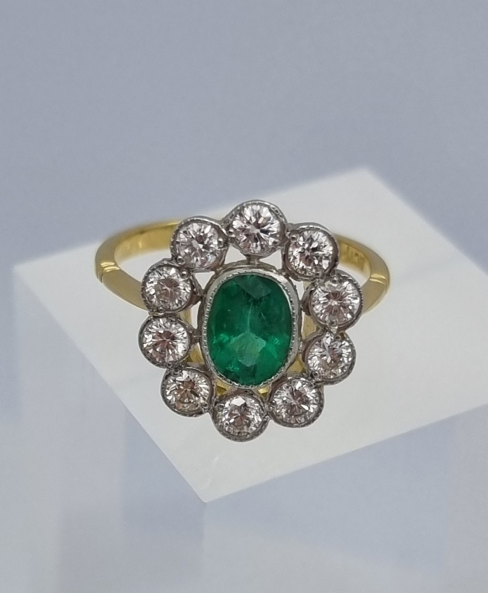 An oval-cut green emerald surrounded by a halo of ten round diamonds in a millgrained cluster setting. View VII