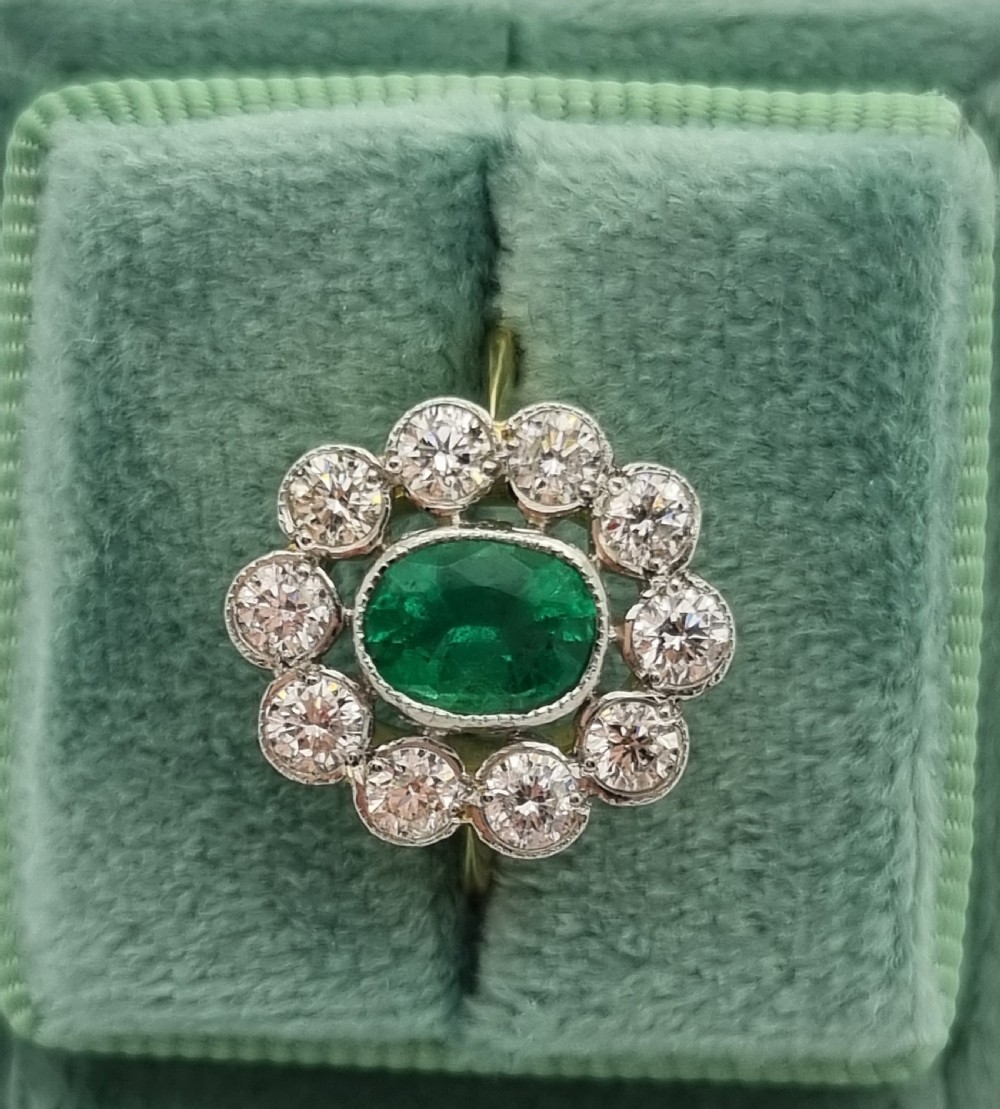 An oval-cut green emerald surrounded by a halo of ten round diamonds in a millgrained cluster setting. View VIII