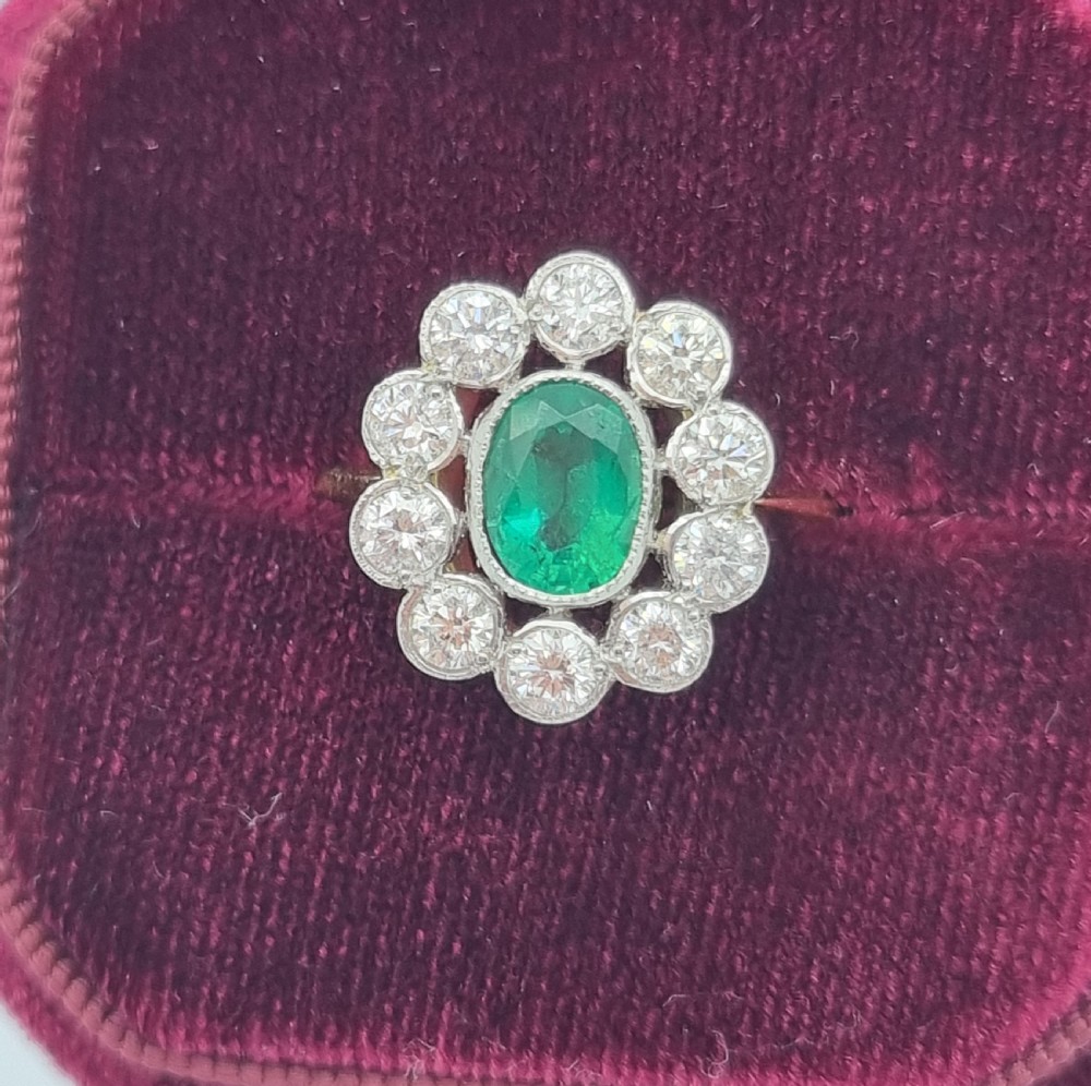 An oval-cut green emerald surrounded by a halo of ten round diamonds in a millgrained cluster setting. View IX
