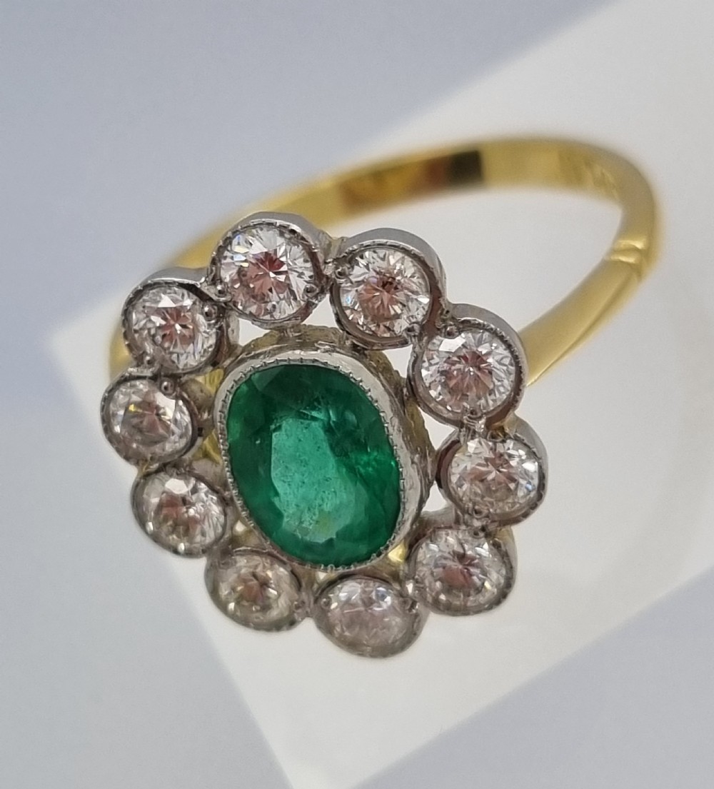An oval-cut green emerald surrounded by a halo of ten round diamonds in a millgrained cluster setting. View X