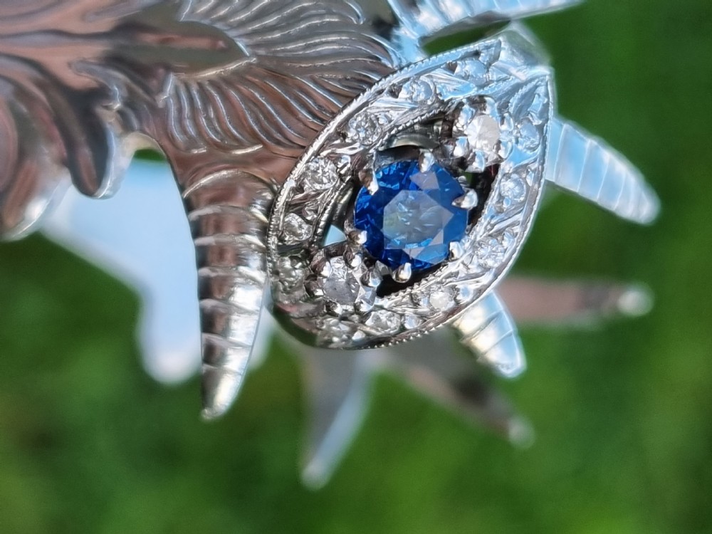 A 14ct gold dress ring featuring a central round blue sapphire surrounded by accent diamonds set in detailed milgrain white gold openwork. View II