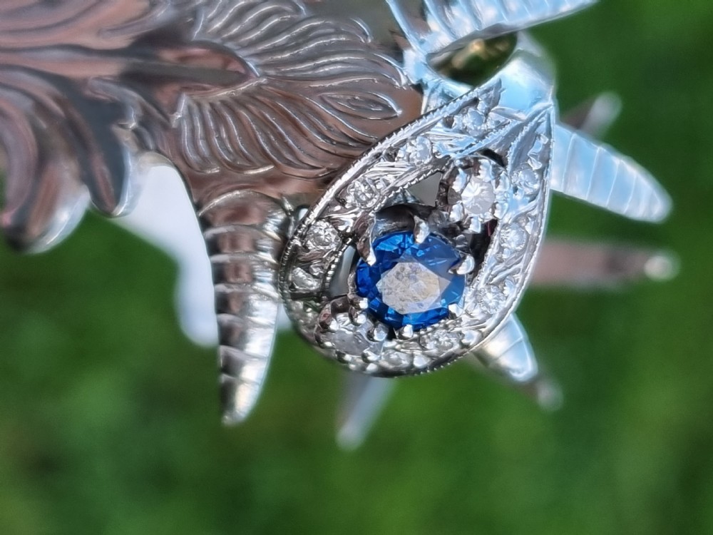 A 14ct gold dress ring featuring a central round blue sapphire surrounded by accent diamonds set in detailed milgrain white gold openwork. View III