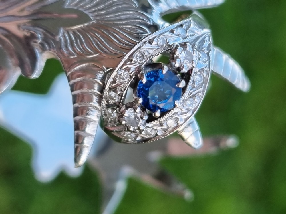 A 14ct gold dress ring featuring a central round blue sapphire surrounded by accent diamonds set in detailed milgrain white gold openwork. View IV