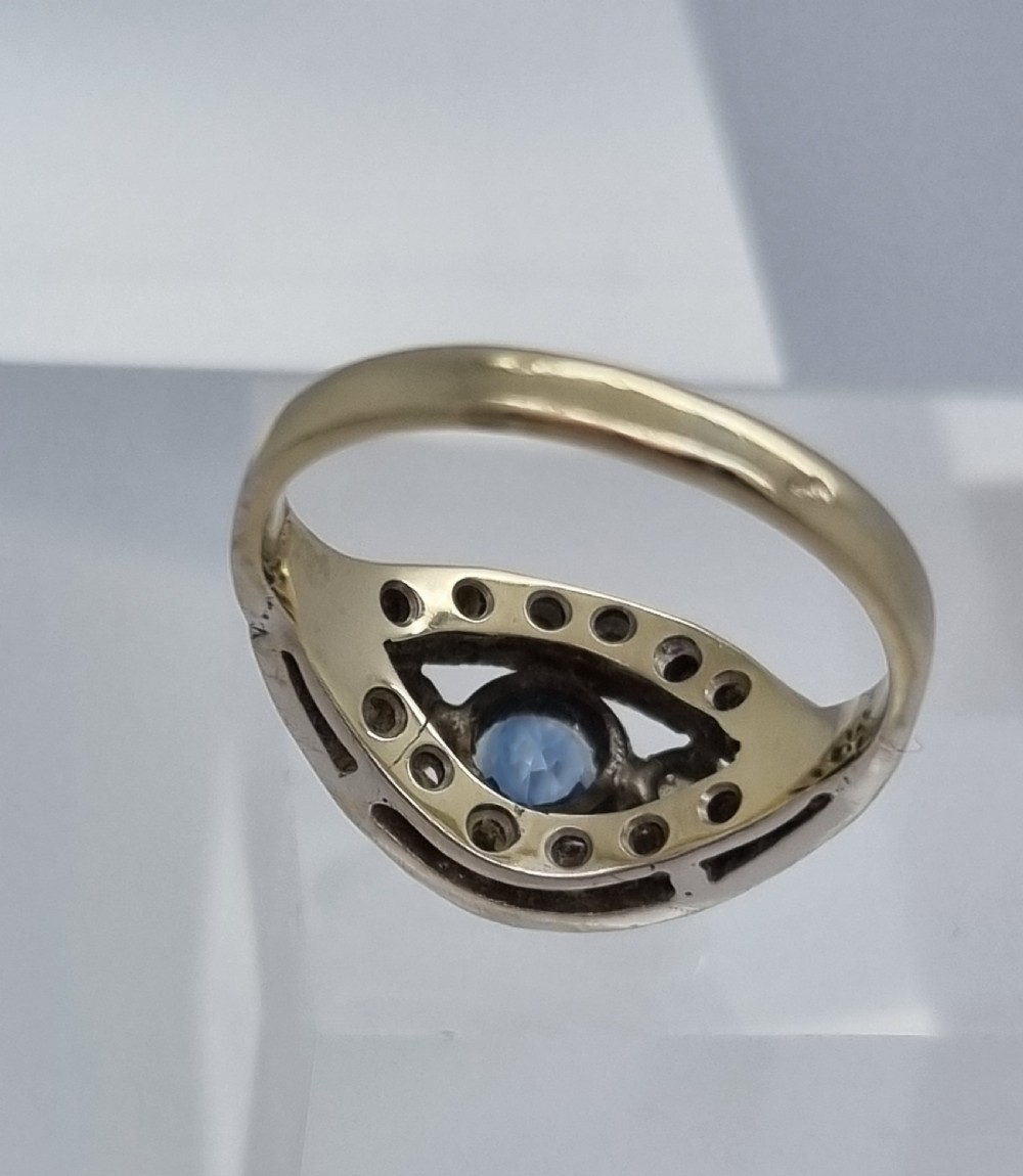 A 14ct gold dress ring featuring a central round blue sapphire surrounded by accent diamonds set in detailed milgrain white gold openwork. View VIII