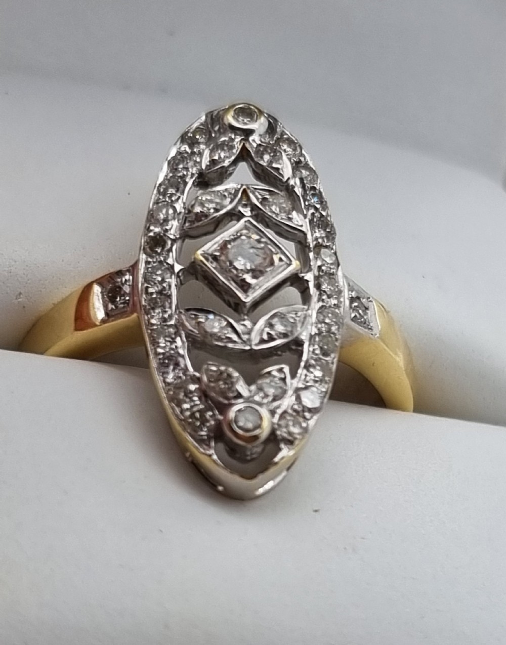 An antique yellow gold ring featuring an elongated oval pierced panel set with small diamonds and a central diamond motif.