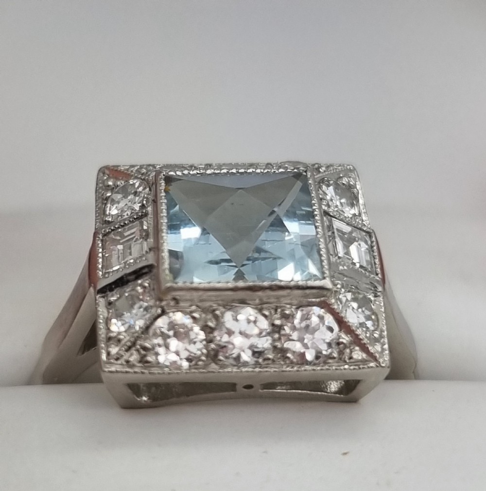 An Art Deco style platinum ring featuring a square central light blue aquamarine surrounded by a geometric border of diamonds with millegrain edging. View VII