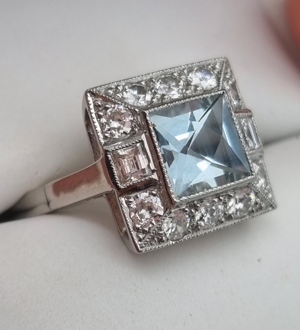 An Art Deco style platinum ring featuring a square central light blue aquamarine surrounded by a geometric border of diamonds with millegrain edging. View IX