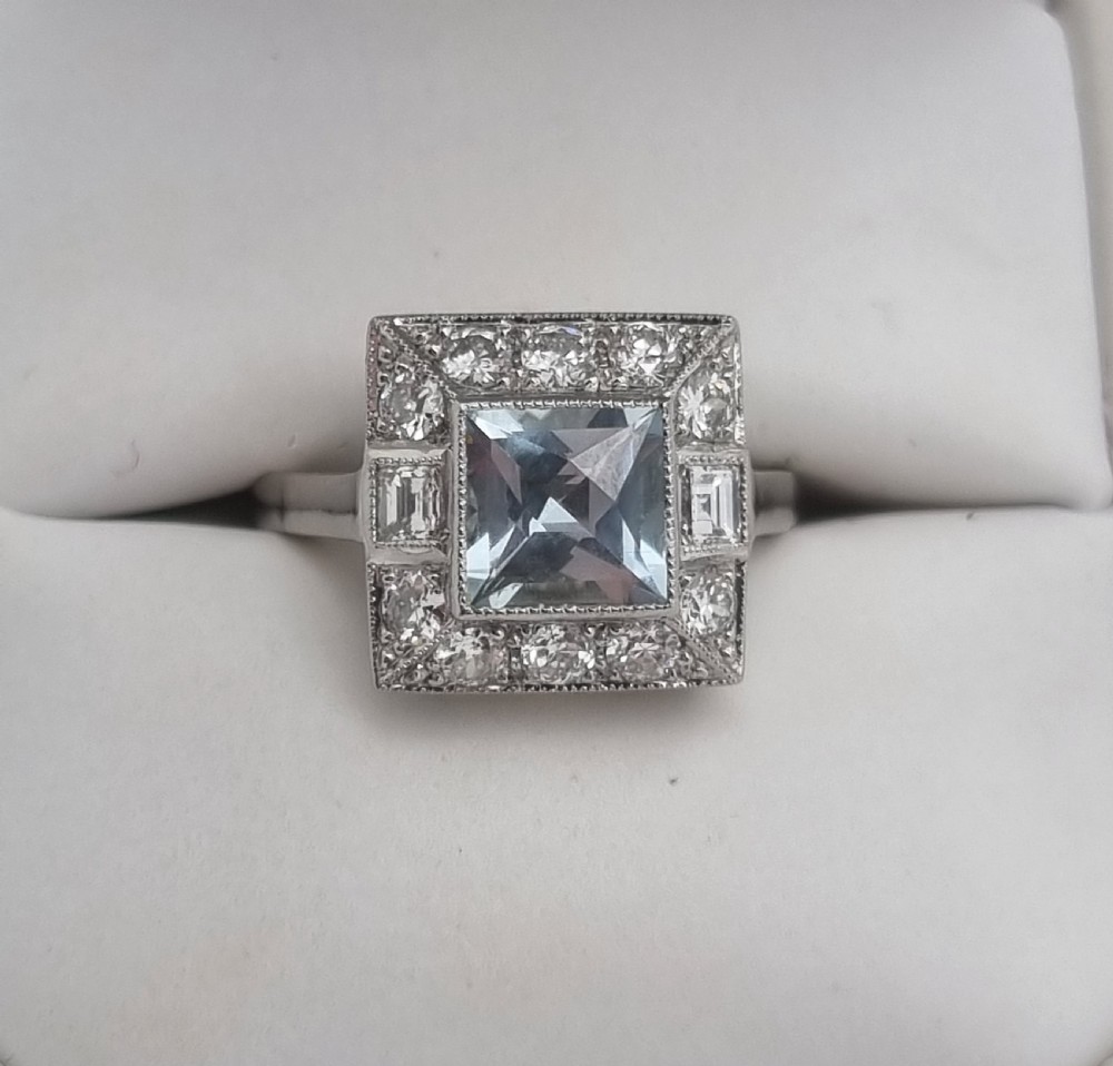 An Art Deco style platinum ring featuring a square central light blue aquamarine surrounded by a geometric border of diamonds with millegrain edging. View X