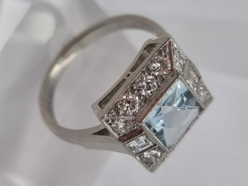 An Art Deco style platinum ring featuring a square central light blue aquamarine surrounded by a geometric border of diamonds with millegrain edging. View XI