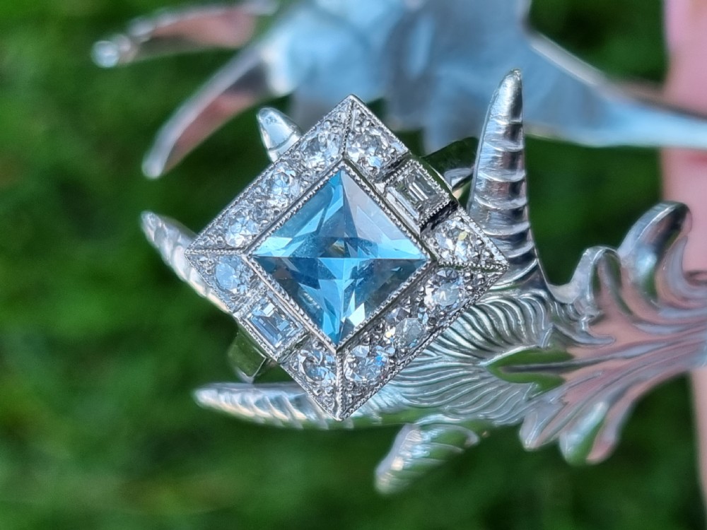 An Art Deco style platinum ring featuring a square central light blue aquamarine surrounded by a geometric border of diamonds with millegrain edging. View XIII