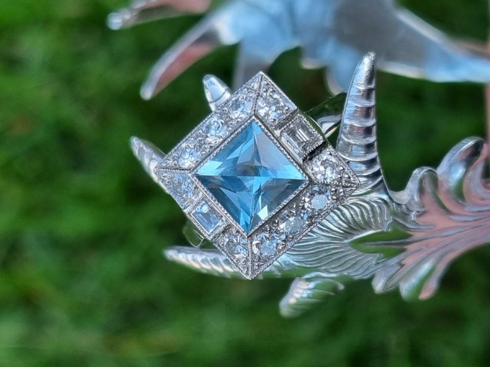 An Art Deco style platinum ring featuring a square central light blue aquamarine surrounded by a geometric border of diamonds with millegrain edging. View XIV