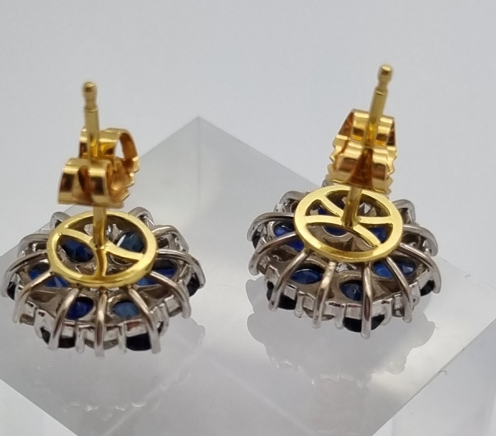A pair of cluster stud earrings featuring deep blue sapphires arranged in a floral motif around a central diamond, set in white metal. View III