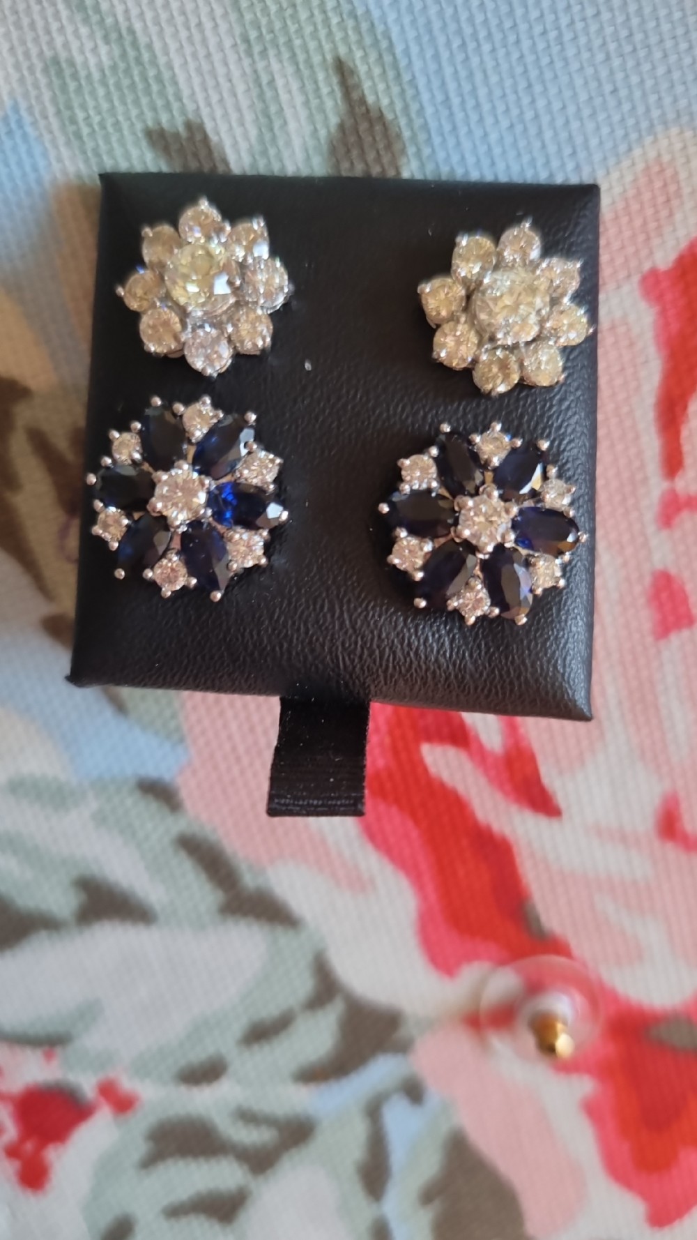 A pair of cluster stud earrings featuring deep blue sapphires arranged in a floral motif around a central diamond, set in white metal. View XVI