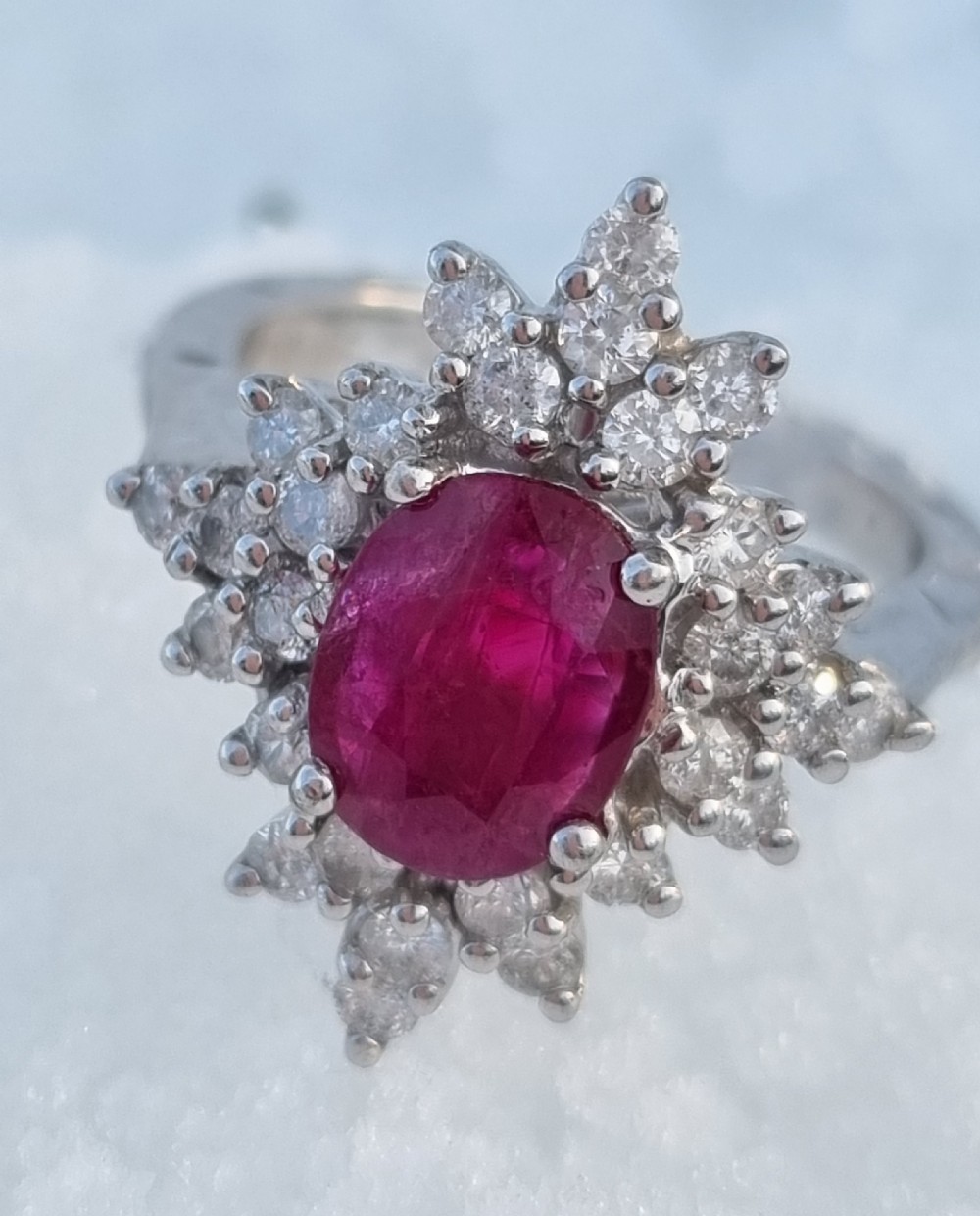 An 18ct white gold cluster ring featuring a central cushion cut ruby surrounded by a starburst halo of diamonds. View V
