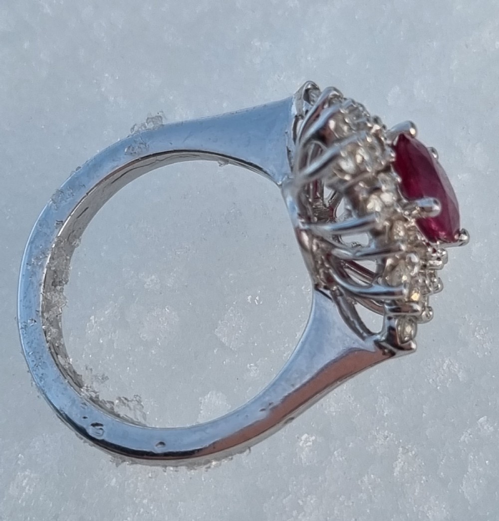 An 18ct white gold cluster ring featuring a central cushion cut ruby surrounded by a starburst halo of diamonds. View VI