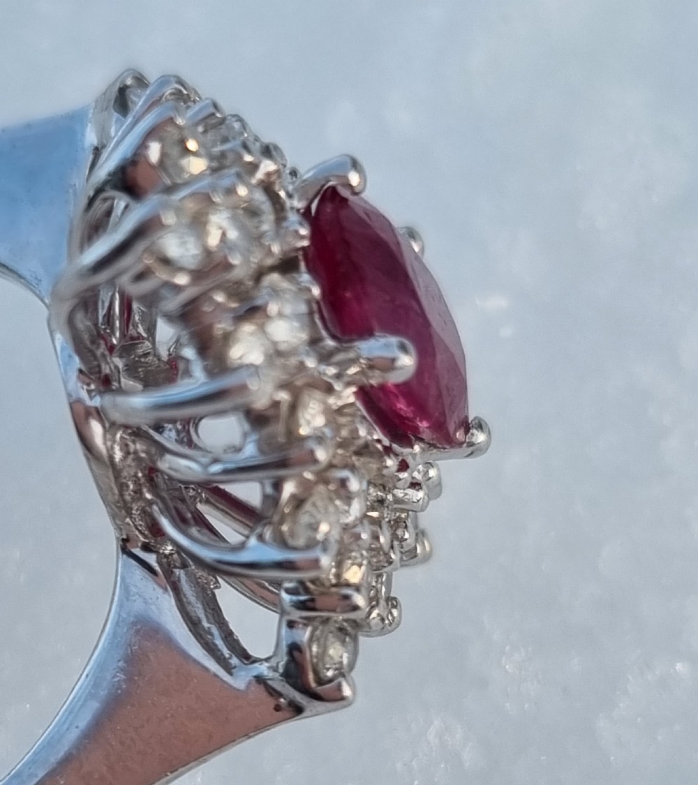 An 18ct white gold cluster ring featuring a central cushion cut ruby surrounded by a starburst halo of diamonds. View VII