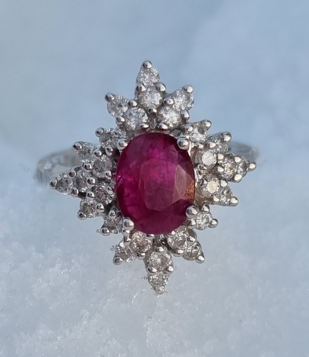 An 18ct white gold cluster ring featuring a central cushion cut ruby surrounded by a starburst halo of diamonds.