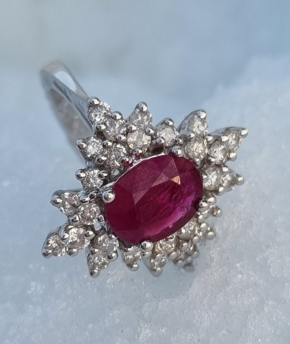 An 18ct white gold cluster ring featuring a central cushion cut ruby surrounded by a starburst halo of diamonds. View IX