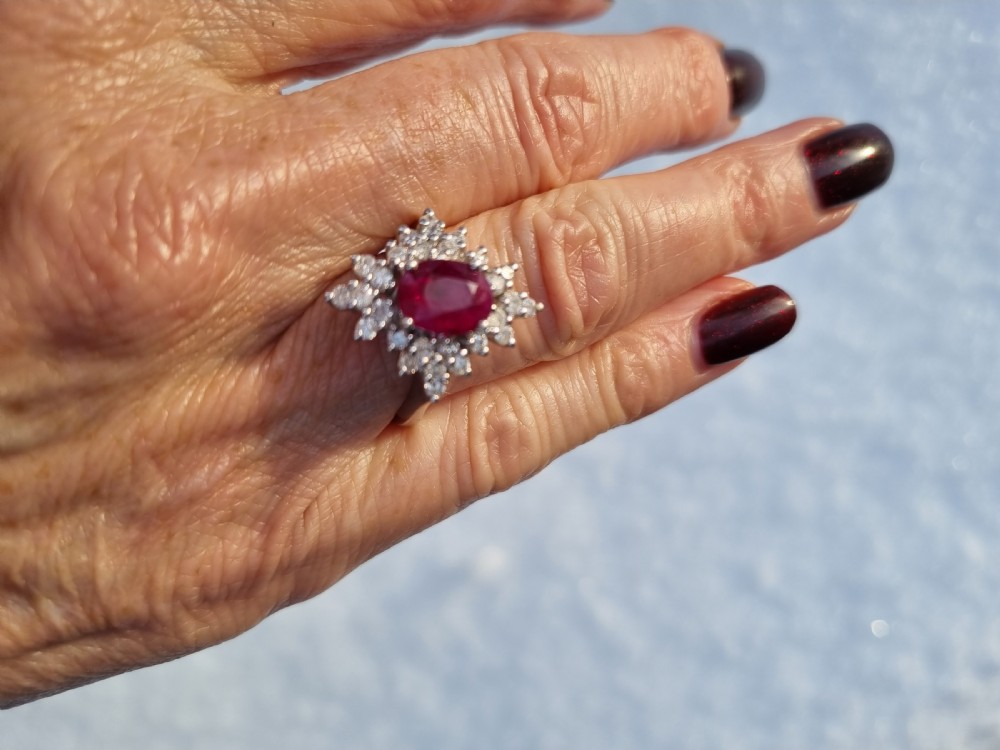 An 18ct white gold cluster ring featuring a central cushion cut ruby surrounded by a starburst halo of diamonds. View XI