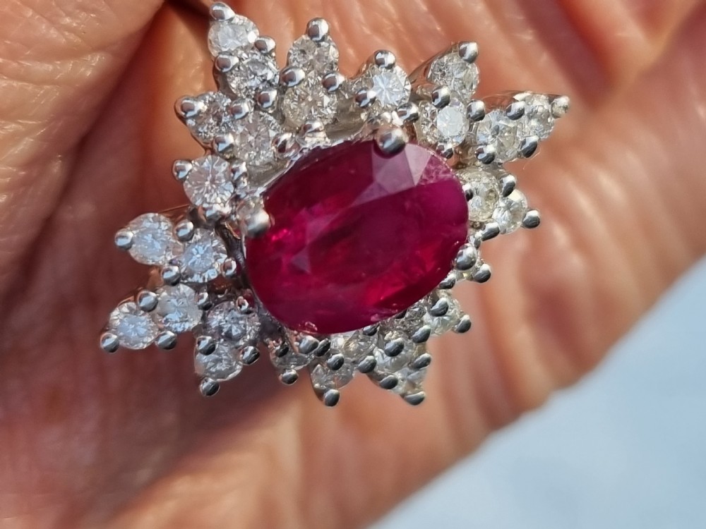 An 18ct white gold cluster ring featuring a central cushion cut ruby surrounded by a starburst halo of diamonds. View XIII