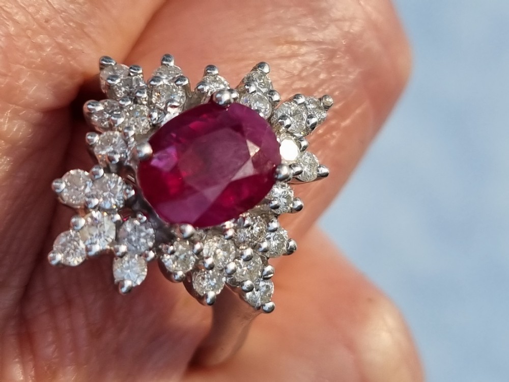 An 18ct white gold cluster ring featuring a central cushion cut ruby surrounded by a starburst halo of diamonds. View XIV