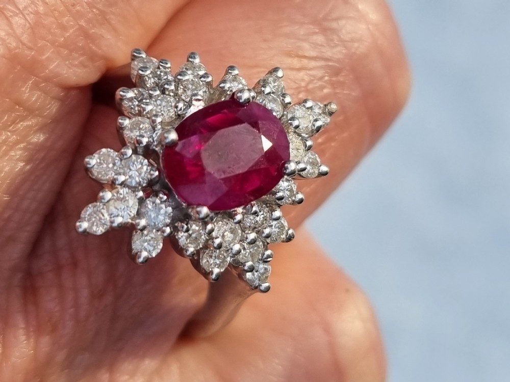 An 18ct white gold cluster ring featuring a central cushion cut ruby surrounded by a starburst halo of diamonds. View XV