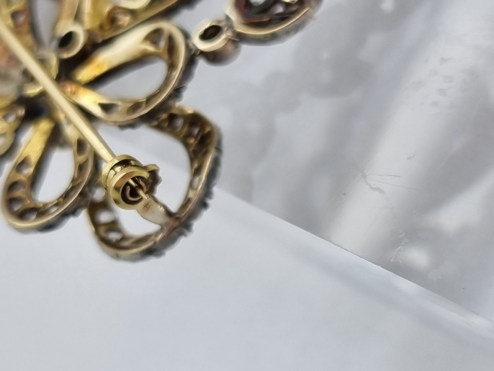 An Edwardian bow and garland design brooch pendant crafted in silver-topped gold, set with diamonds and teardrop blue sapphires. View VI