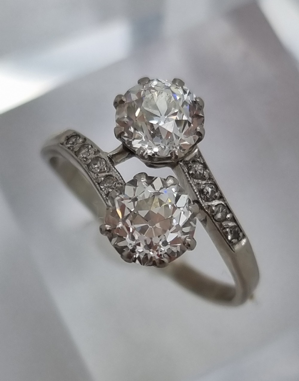 An Art Deco platinum twist ring featuring two central round diamonds in a crossover setting with diamond-set shoulders. View VI