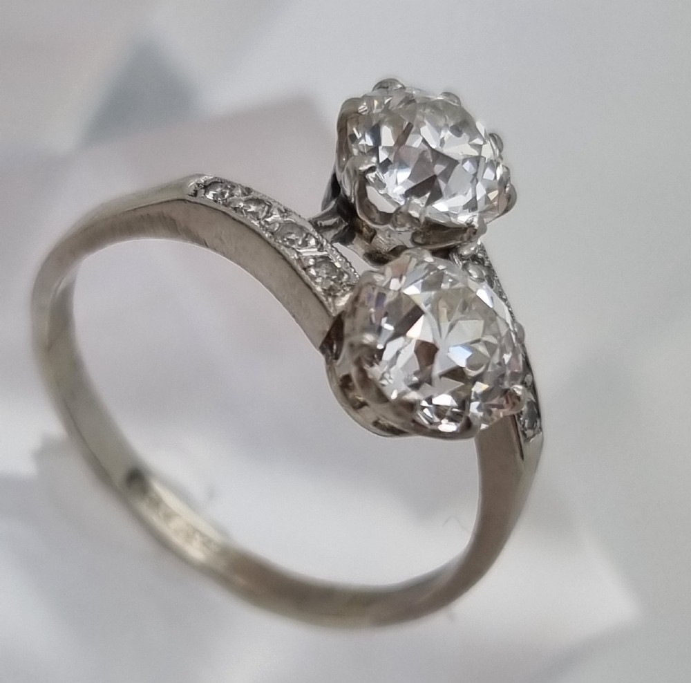 An Art Deco platinum twist ring featuring two central round diamonds in a crossover setting with diamond-set shoulders. View VII