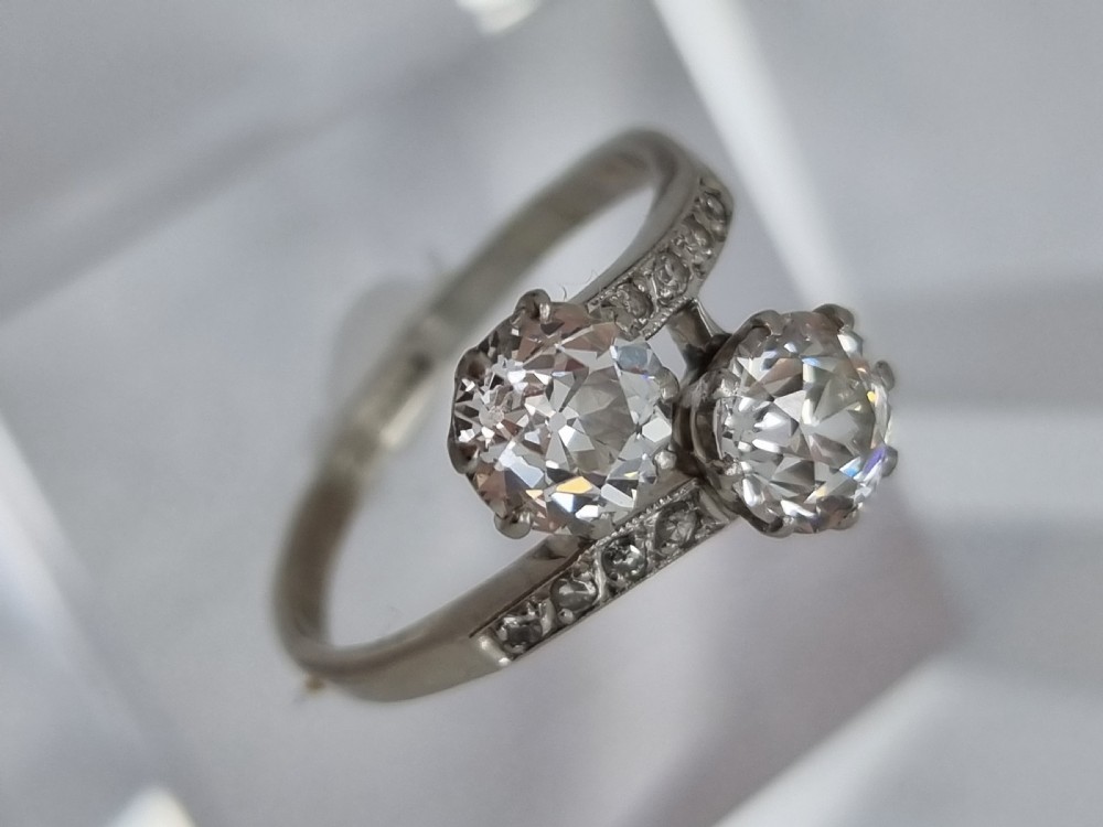 An Art Deco platinum twist ring featuring two central round diamonds in a crossover setting with diamond-set shoulders. View IX